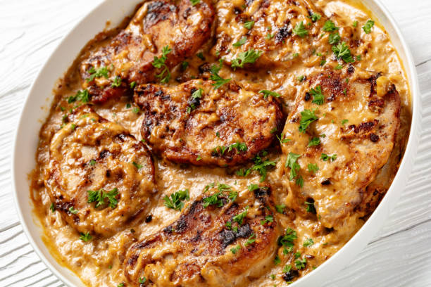 A delicious dish of pork chops in creamy sauce, garnished with parsley, served in a round white dish.
