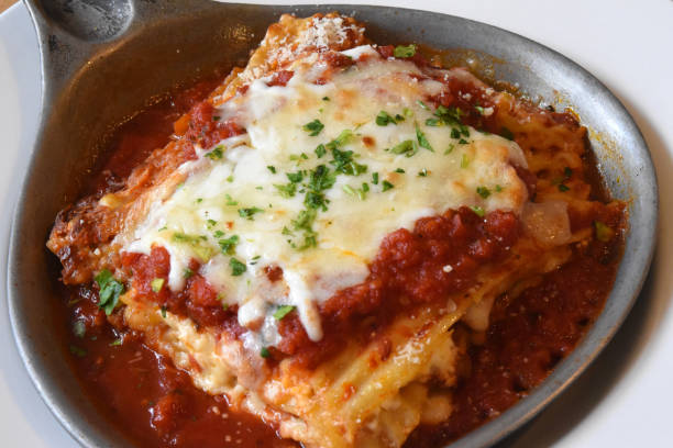 A delicious serving of lasagna topped with melted cheese and garnished with parsley in a small steel dish.