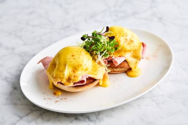 Two eggs Benedict on a white plate with garnish, served on a marble table.