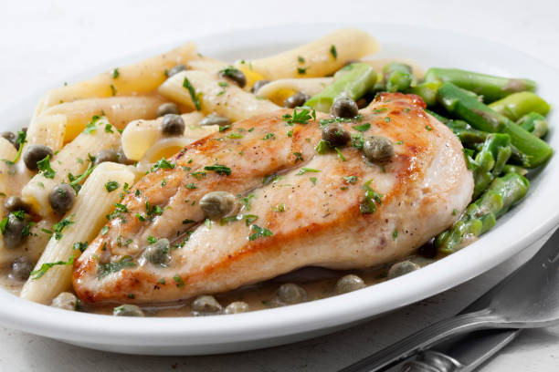 Grilled chicken breast served with pasta and green vegetables on a white plate.