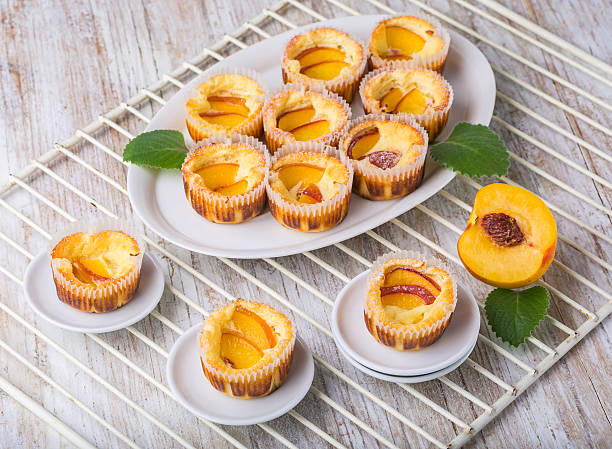 A selection of peach cupcakes arranged on a plate, with some on small white dishes and a sliced peach on the side.