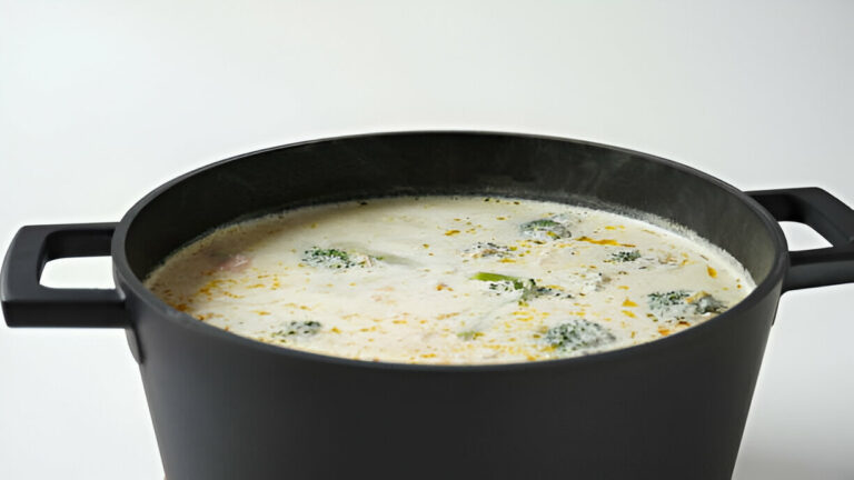 A large black pot filled with creamy soup containing broccoli, viewed from the top
