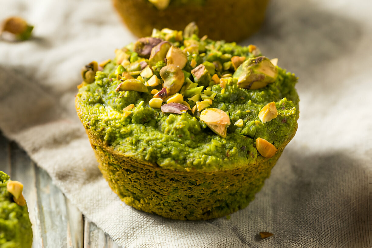 Green muffin topped with chopped nuts on a textured cloth