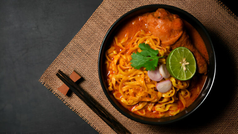 A bowl of rich chicken curry noodles topped with cilantro, lime, and shallots.