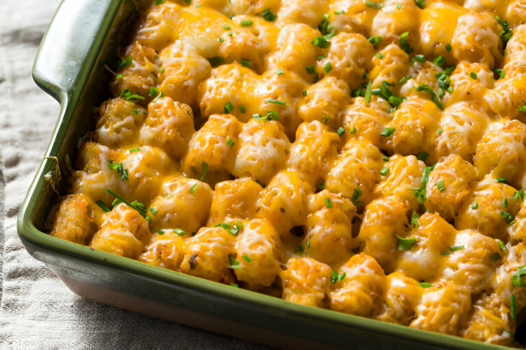 A close-up view of a cheesy tater tot casserole topped with chopped green onions in a green baking dish.