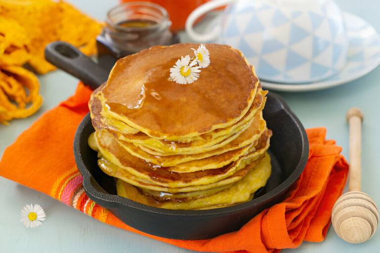 A stack of pancakes drizzled with syrup, garnished with a small flower, served in a cast iron skillet.