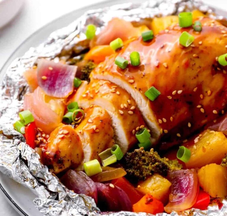 Oven-baked chicken breast in a foil with vegetables, topped with sauce and green onions
